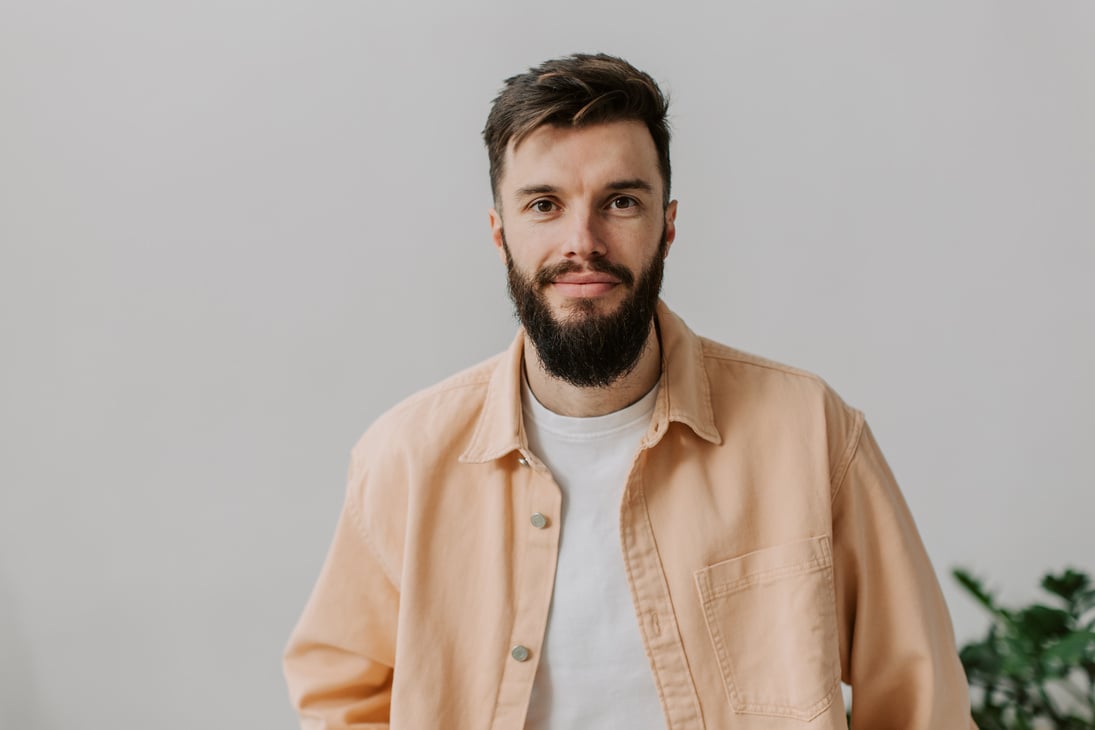 a person with a beard standing in front of a gray background